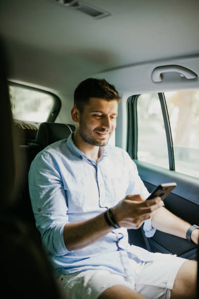 istock Handsome man using a smart phone and smiling while sitting on back seat in the car 1210559080