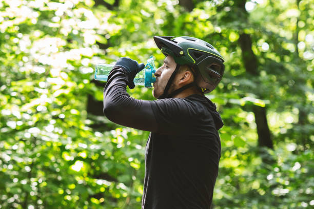 istock Male cyclist drinking water while riding in forest 1210560046