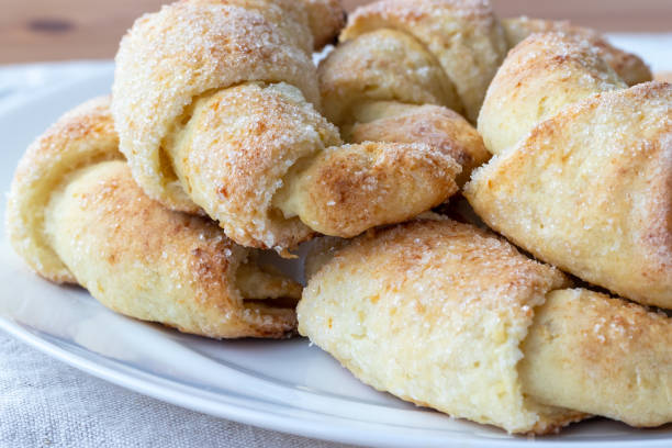 des croissants givrés au sucre d’une pâte de fromage cottage sur une assiette blanche sur une nappe de lin gris vient d’être sorti du four. collation de thé pour le petit déjeuner. le processus de fabrication de bagels caillés ou croissants - twisted cheese biscuit pastry photos et images de collection