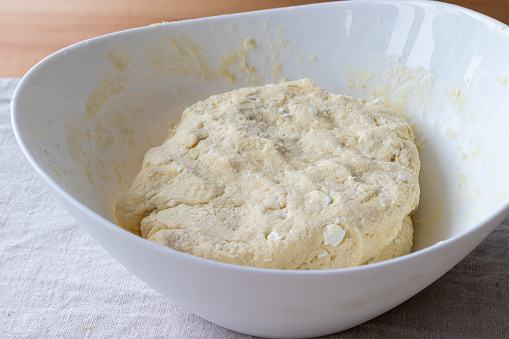 Raw curd dough with bits of cottage cheese in a white bowl on a linen tablecloth on a wooden table. The process of making curd bagels or croissants