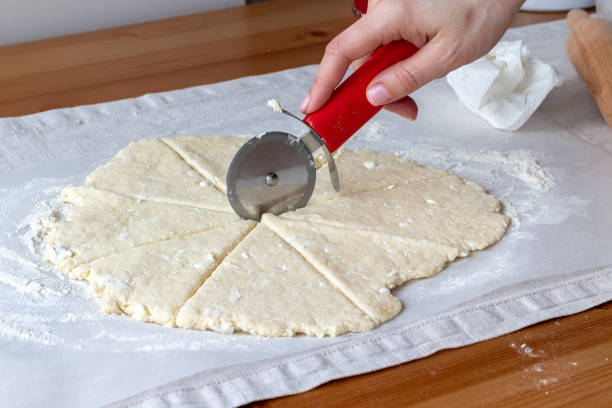 istock Hand cuts rolled raw curd dough with a round pizza knife into eight triangles on baking paper on a linen tablecloth on a wooden table. The process of making curd bagels or croissants 1210562634