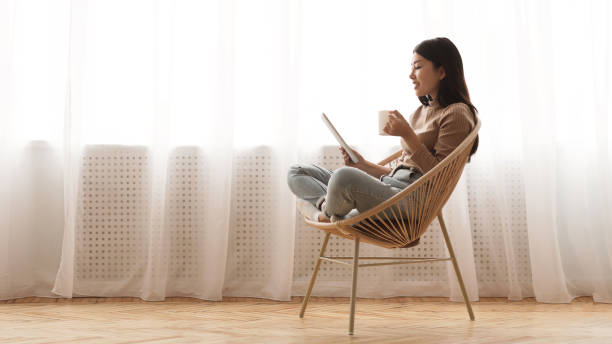 istock Free time. Girl using tablet and drinking coffee in wicker chair 1210562865