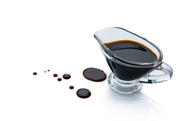 Balsamic vinegar in a gravy boat isolated on white background High angle view of balsamic vinegar in a gravy boat isolated on reflective white background. Some vinegar drops are spilled on the background beside the container. The composition is at the right of an horizontal frame leaving useful copy space for text and/or logo at the left. Predominant colors are black and white. High resolution 42Mp studio digital capture taken with Sony A7rII and Sony FE 90mm f2.8 macro G OSS lens balsamic vinegar stock pictures, royalty-free photos & images