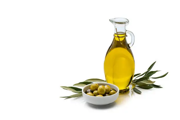 Extra virgin olive oil containers and olives in a white bowl isolated on reflective white background. Olive tree branches complete the composition. The composition is at the right of an horizontal frame leaving useful copy space for text and/or logo at the left. Predominant colors are yellow, green and white. High resolution 42Mp studio digital capture taken with Sony A7rII and Sony FE 90mm f2.8 macro G OSS lens