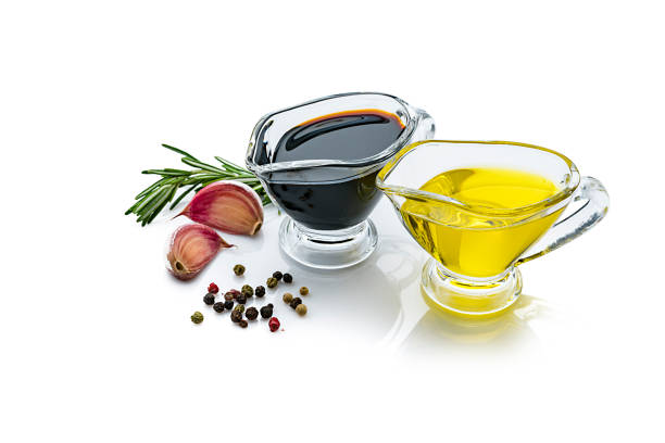 Olive oil and balsamic vinegar containers isolated on reflective white background Extra virgin olive oil and balsamic vinegar in glass gravy boats isolated on reflective white background. Rosemary twigs, garlic cloves, and mixed peppercorns are around the containers and complete the composition. The composition is at the right of an horizontal frame leaving useful copy space for text and/or logo at the left. Predominant colors are yellow, black and white. High resolution 42Mp studio digital capture taken with Sony A7rII and Sony FE 90mm f2.8 macro G OSS lens balsamic vinegar stock pictures, royalty-free photos & images
