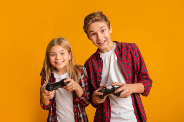 istock Kids Leisure. Brother And Sister With Joysticks Posing Over Yellow Background 1210565607
