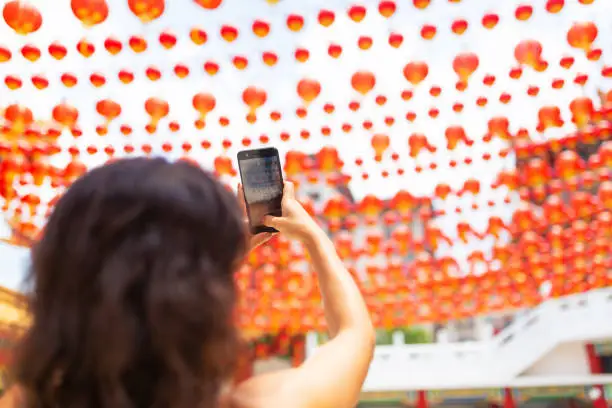 Photo of A tourist girl photographs the festive New Year decorations with Chinese lanterns of the Chinese temple