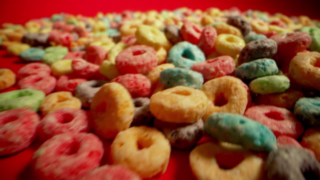 Macro Close-Up Wide Angle Moving Shot of Sugary Colorful Fruit Loop American Breakfast Cereal Spread Out on a Red Background