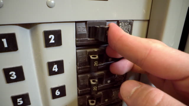 Close-Up Shot of Male Caucasian Hand Switching On and Off a 20-Amp Electrical Breaker Panel from a Commercial Building Install