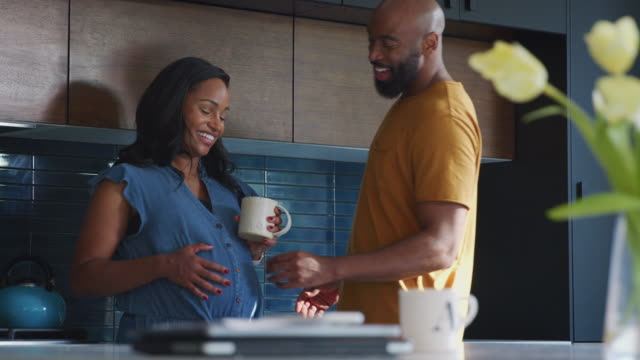 Loving Hispanic Husband With Pregnant Wife At Home In Kitchen Together