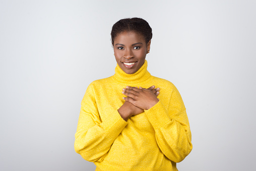 Cheerful woman holding hands on chest. Beautiful happy young African American woman standing with hands near heart and smiling at camera. Love concept