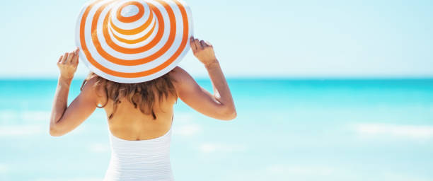 mujer joven con sombrero de pie en la playa. vista trasera - women summer hat beach fotografías e imágenes de stock