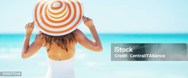 Young Woman In Hat Standing On Beach Rear View Stock Photo - Download Image Now - Women, Beach, Sun