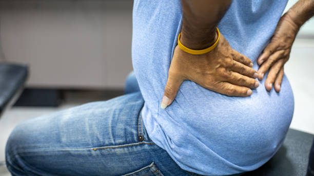 jovem que sofre de dor nas costas enquanto senta em uma cadeira , síndrome do escritório - physical injury backache occupation working - fotografias e filmes do acervo