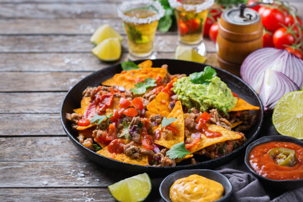 Chips nachos with beef, guacamole, chili, cheese salsa, tequila Yellow corn tortilla chips nachos with ground beef, mince, guacamole, red hot jalapeno chili salsa and cheese sauce with tequila on a wooden table. hot mix plant stock pictures, royalty-free photos & images