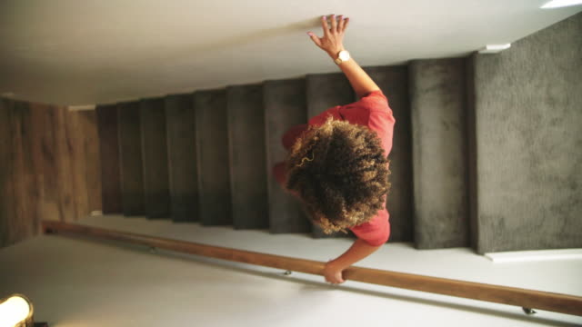 Slow Motion Directly Above Shot of a Woman of Mixed Race Walking down Carpeted Stairs in a Home, Using the Wall and a Hand Rail for Support