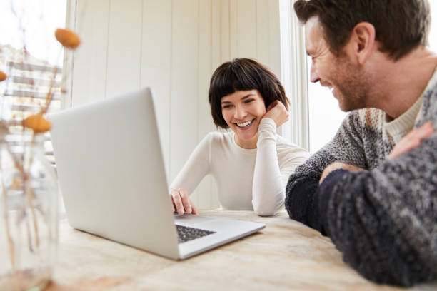 istock Laughing young couple using a laptop at their kitchen table 1210584839