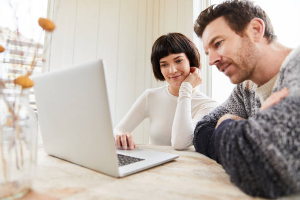 istock Smiling young couple using a laptop at their kitchen table 1210585159