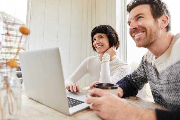 istock Young couple laughing while working on a laptop at their kitchen table 1210585275