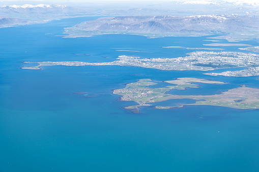 Keflavik, Iceland airport bird's eye aerial high angle view of Reykjavik city from airplane window above and colorful ocean water