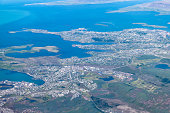 Keflavik, Iceland airport and urban city bird's eye aerial high angle view of Reykjavik from airplane window above and colorful ocean water
