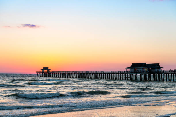 napoli, florida tramonto crepuscolo nel golfo del messico con molo molo all'orizzonte e silhouette onde dell'oceano vista - florida naples florida pier beach foto e immagini stock