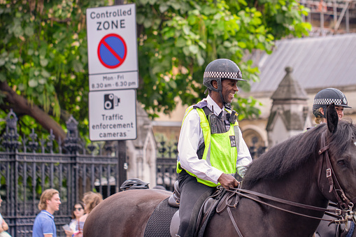 31st August, 2019 - Happy laughing black metropolitan police officer on horseback patrols the crowds of tourists outside the Houses of Parliament in Westminster, London, UK