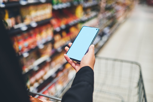 Cropped shot of a woman using a smartphone while shopping in a grocery store