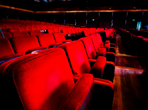 a row of empty red velvet armchairs inside an auditorium.
