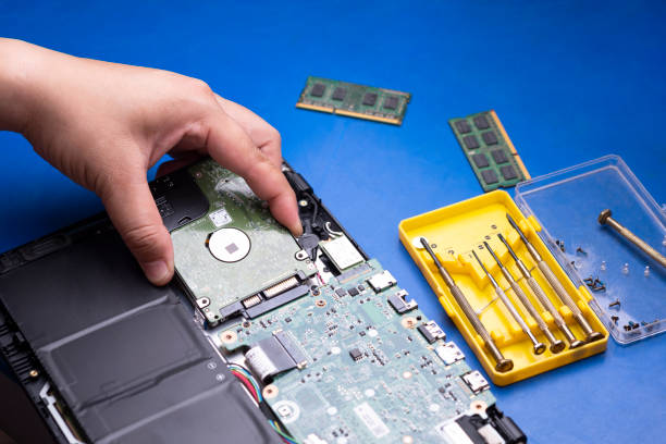 hand holding hard disk to install on motherboard of laptop Selective focus at technician hand holding hard disk to install on motherboard of laptop with 2 access memory[RAM] and screwdrivers in yellow box on blue tabletop, upgrading quality of laptop concept installing laptop ram stock pictures, royalty-free photos & images