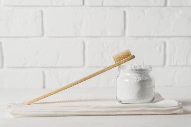 Bamboo toothbrush with a white towel and powder for cleaning teeth in a bowl on a background of a light brick wall. stock photo