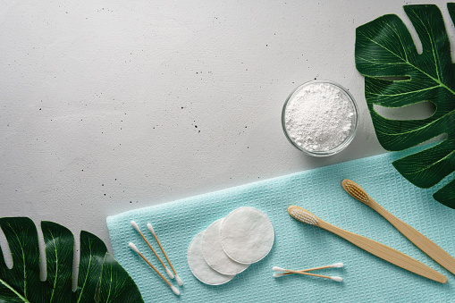 Zero waste and minimalism concept. Two bamboo toothbrushes, tooth powder, cotton pads and sticks on a light gray concrete background. Top view, copy space. No plastic.