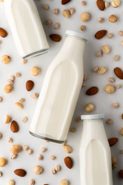 istock Three glass bottles with milk and scattered macadamia nuts, almonds, chickpeas on a light gray concrete surface. 1210599021