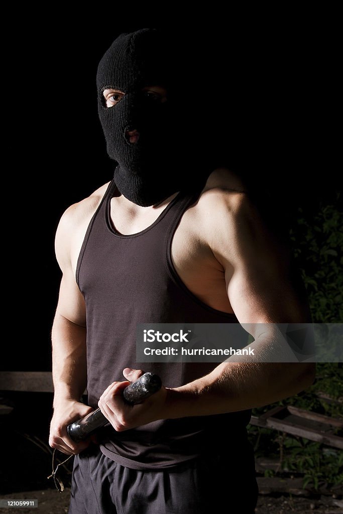 Gangster with baton outdoors at night Big athletic thug in black sportive costume and black mask armed with police baton Adult Stock Photo
