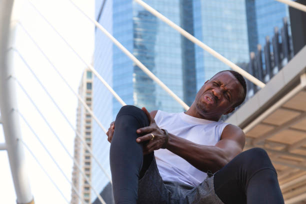 african american sportsman uses two hands holding his knee after feeling pain and injury in hard practicing running exercise. health care, sport and insurance concept. - twisted ankle fotos imagens e fotografias de stock