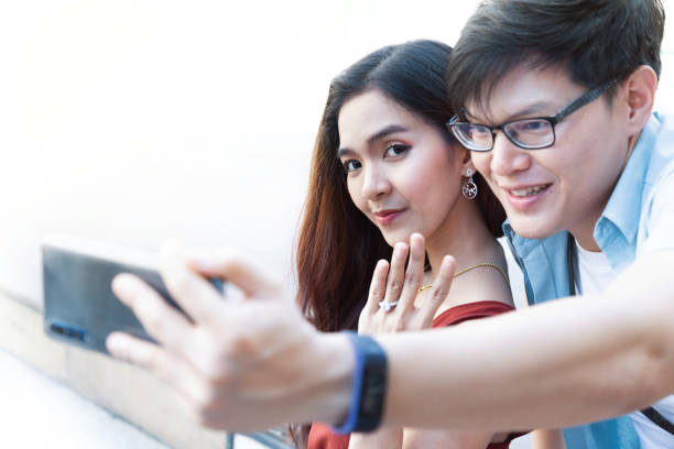 istock young asian man using smartphone taking photos with his girlfriend after engaged proposal and smiling happy woman and showing her wedding ring. happy loving couple on engagement day 1210600076