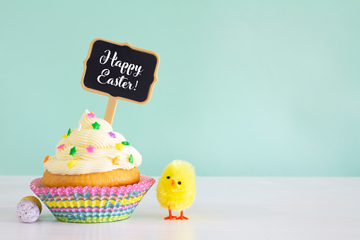 A buttercream cupcake with sprinkles and a sign saying Happy Easter.