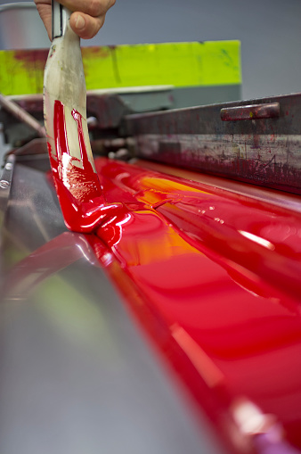 closeup of spatula that spreads the red color on the roller of the offset machine