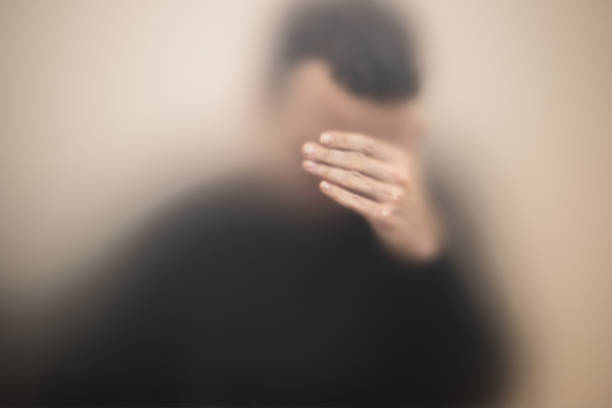 istock Stressed man covers his face with hand behind glass 1210608076