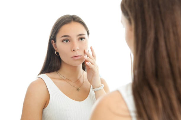 Young Woman in Front of a Mirror Looking at her Acne Scars stock photo