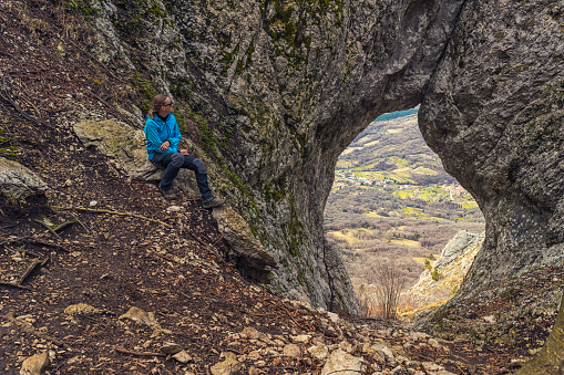 Hiking woman sitting at large natural window - The Otlica Natural Windov in Vipava Valley -in rocky mountain. View throe window on small city of Ajdovščina. Well known spot for wonderful paragliding and wine making.