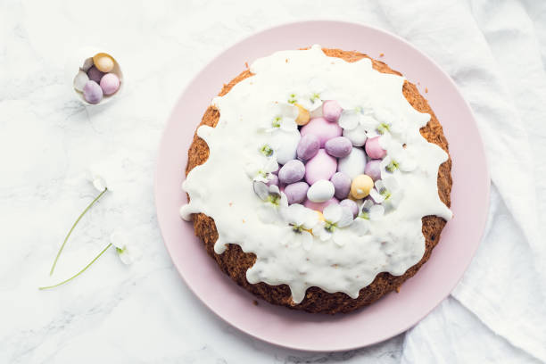 Glazed easter cake with flowers and candy Glazed easter cake decorated with flowers and mini chocolate eggs candy on white marble background. Happy Easter Holidays. Top view. Copy space. easter cake stock pictures, royalty-free photos & images