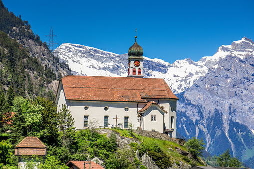 Wassen, Switzerland - June 2, 2019: The church of Wassen is seen by train on today's historic route across the Gotthard from a total of three different directions. The church in Uri canton was completed in 1734 and is now a cultural asset of national importance.