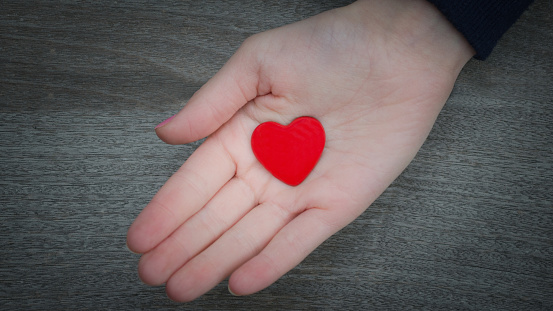 Kids hand holding red heart over solid wooden background in a conceptual image of love, family and care.