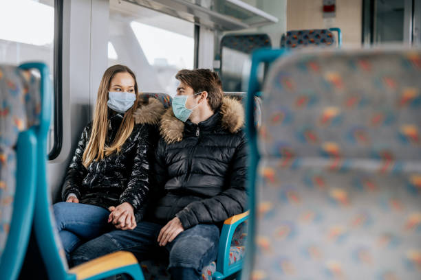 istock Young couple is sitting on a train wearing protective face masks and looking at each other 1210625793
