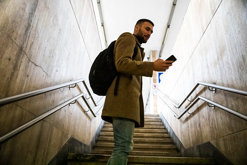 Young Traveler Stopping in the middle of the Staircase to Check his Smart Phone - Stock Photo