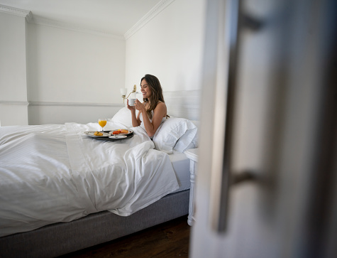 Happy woman eating breakfast in bed at her hotel room - lifestyle concepts