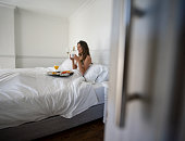 Happy woman eating breakfast in bed at her hotel room