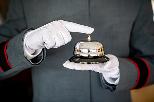 Close-up on a bellhop working at a hotel holding a service bell wearing a uniform and gloves