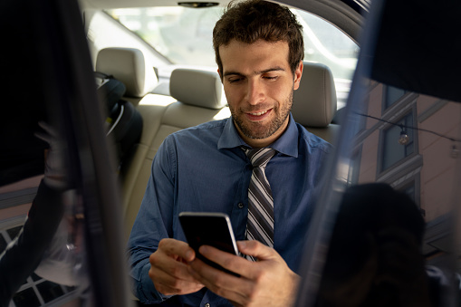 Portrait of a business man texting on his cell phone while riding on a car